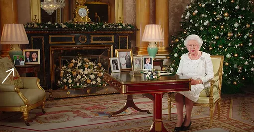 Королева Елизавета II в своем кабинете (слева — фото принца Гарри и Меган Маркл)